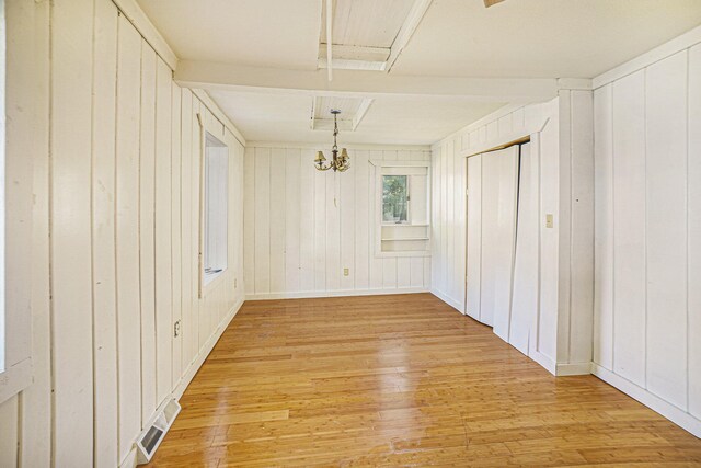 unfurnished room with light hardwood / wood-style floors, wooden walls, and a notable chandelier