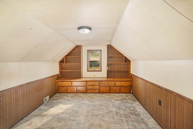 bonus room with wood walls, built in shelves, vaulted ceiling, and light carpet