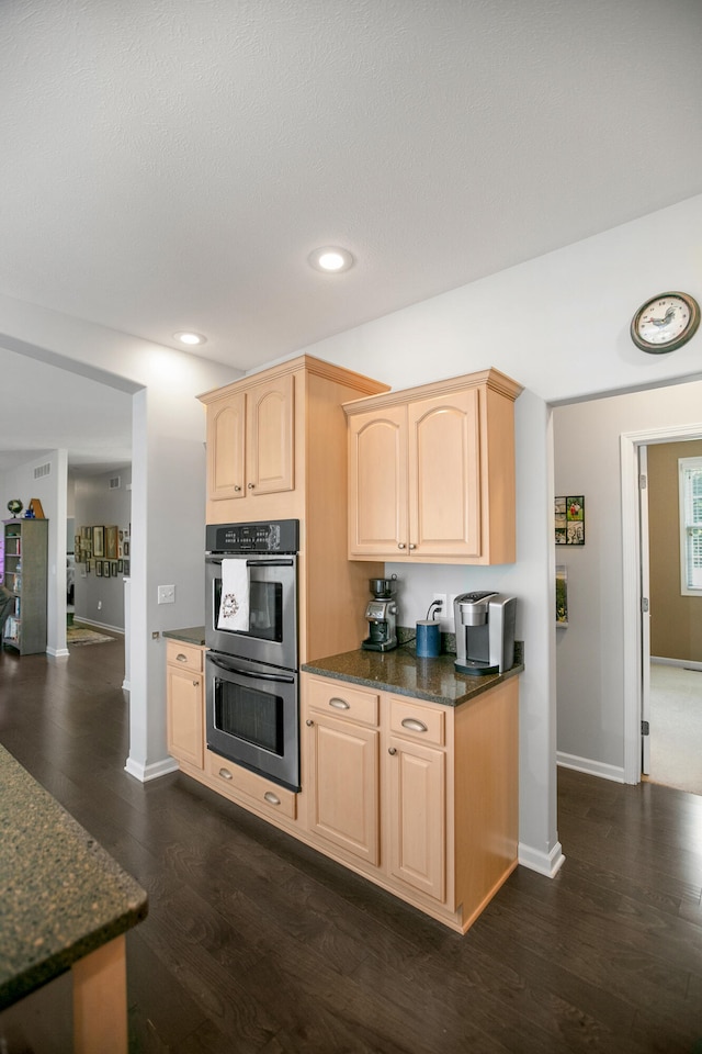 kitchen featuring dark stone countertops, double oven, light brown cabinets, and dark wood-type flooring