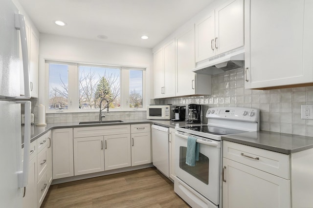 kitchen with white appliances, white cabinets, under cabinet range hood, and a sink
