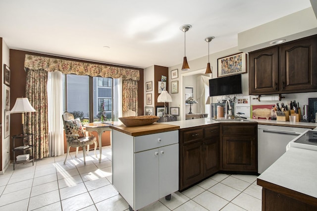 kitchen featuring light tile patterned floors, a peninsula, a sink, dark brown cabinetry, and stainless steel dishwasher