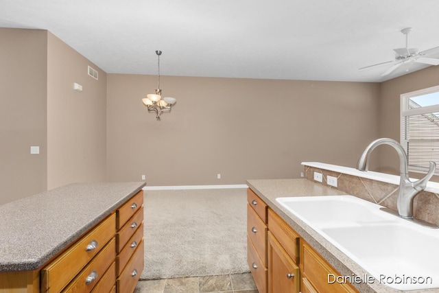 kitchen featuring light carpet, ceiling fan with notable chandelier, sink, a center island, and hanging light fixtures