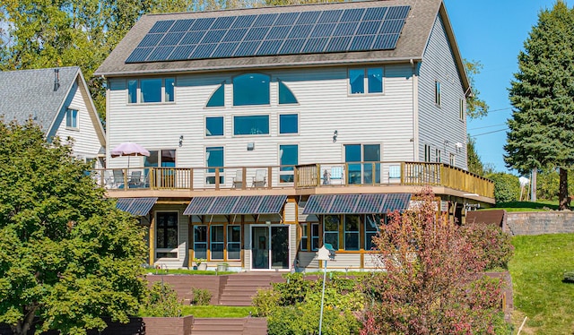back of house with roof with shingles and roof mounted solar panels