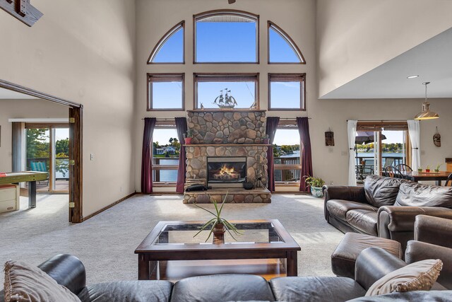 carpeted living room featuring a towering ceiling, a water view, and a fireplace