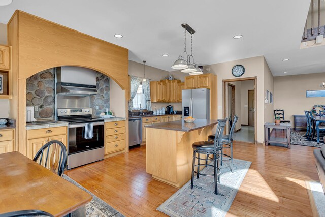 kitchen with a kitchen island, light brown cabinets, stainless steel appliances, pendant lighting, and light hardwood / wood-style flooring