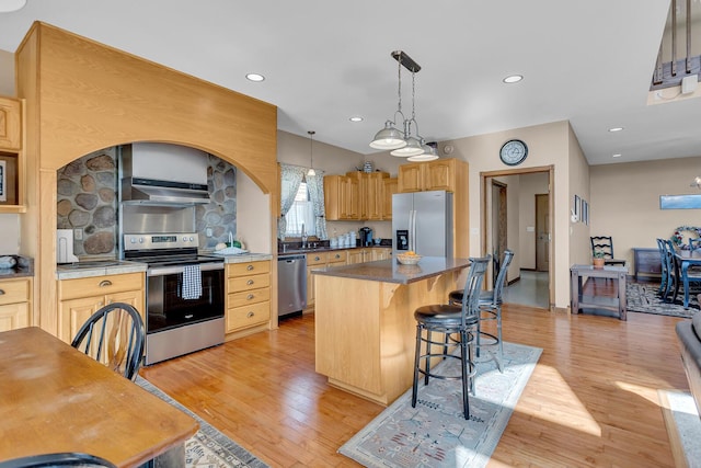 kitchen with light wood-style floors, under cabinet range hood, a kitchen island, and stainless steel appliances