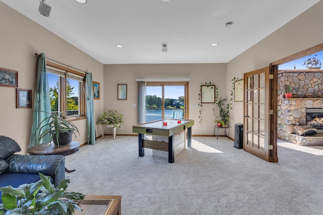 game room featuring light carpet, a stone fireplace, and a water view