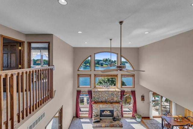 living room featuring a ceiling fan, a stone fireplace, a water view, a high ceiling, and recessed lighting