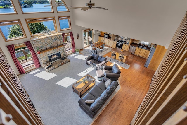 living area featuring a fireplace, a towering ceiling, light wood-type flooring, and ceiling fan