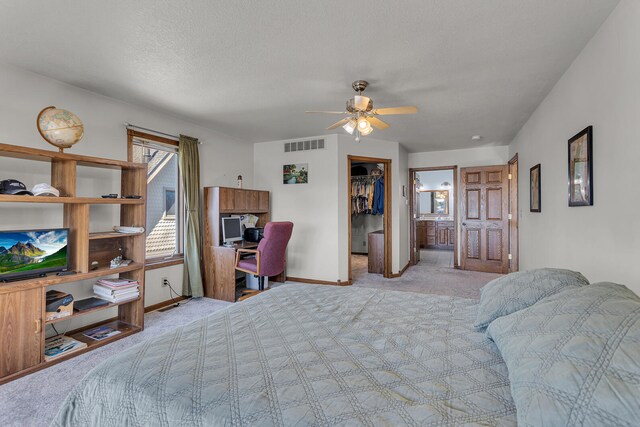 bedroom with ceiling fan, a closet, a walk in closet, light colored carpet, and a textured ceiling