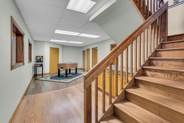 staircase featuring baseboards, wood finished floors, and a drop ceiling