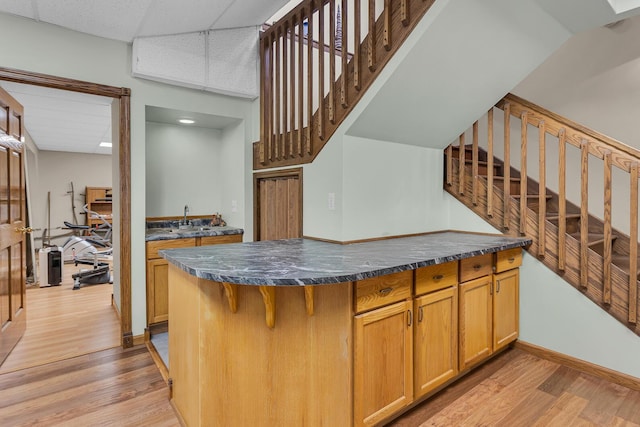 kitchen featuring light wood finished floors, dark countertops, a breakfast bar, and brown cabinetry