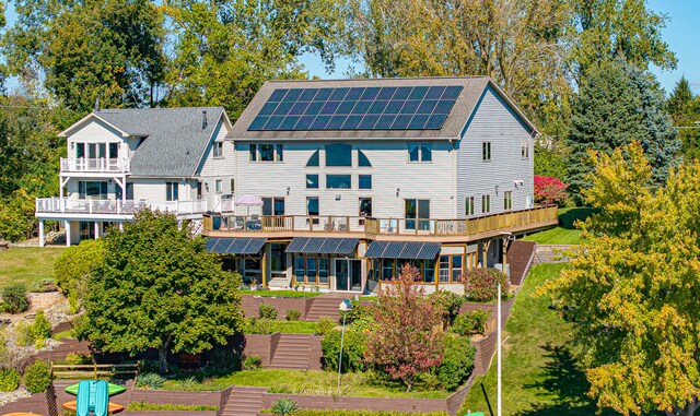 back of house featuring solar panels, a wooden deck, and a lawn