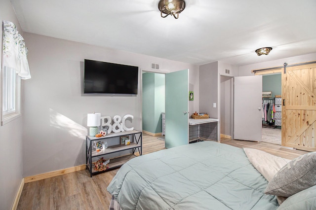 bedroom featuring a walk in closet, light wood-type flooring, a barn door, and a closet