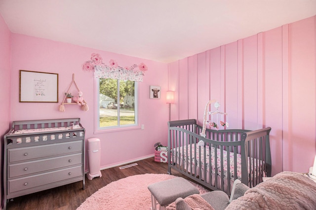 bedroom with a nursery area and dark wood-type flooring