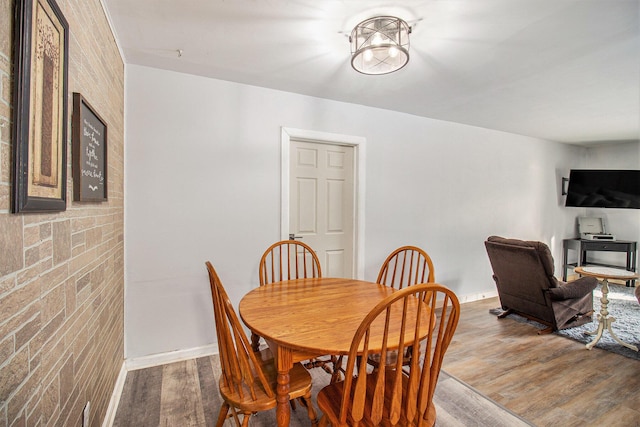 dining room with wood-type flooring and brick wall