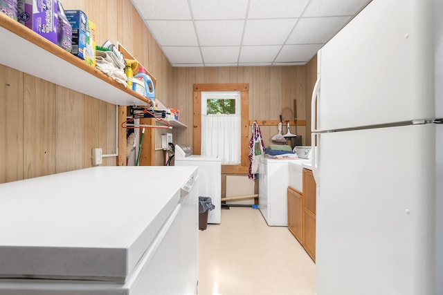 kitchen with a drop ceiling, wooden walls, white refrigerator, and washer and clothes dryer