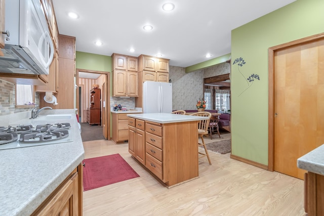 kitchen featuring a kitchen breakfast bar, light hardwood / wood-style floors, white appliances, and a kitchen island