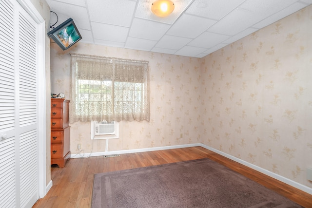 unfurnished room with wood-type flooring, a drop ceiling, and a wall mounted AC