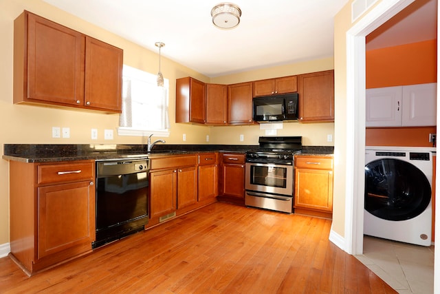 kitchen with light hardwood / wood-style floors, dark stone countertops, black appliances, washer / dryer, and decorative light fixtures