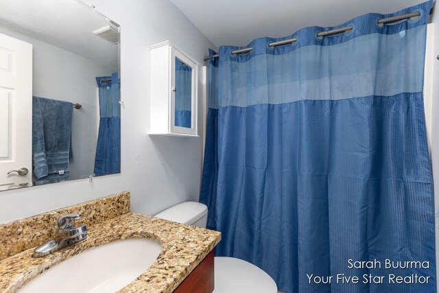 bathroom with curtained shower, vanity, and toilet