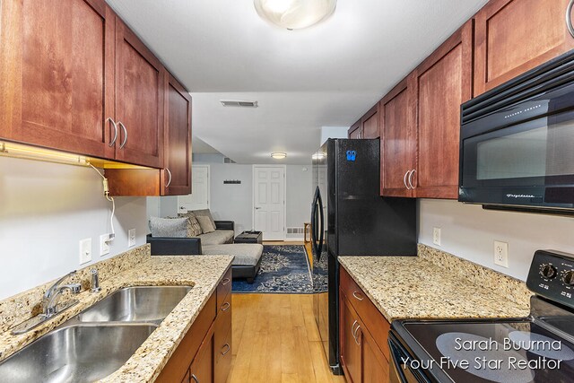 kitchen with light stone counters, light hardwood / wood-style flooring, sink, and black appliances