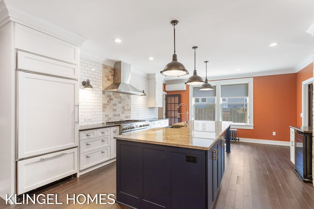 kitchen with light stone countertops, white cabinets, wall chimney range hood, and sink