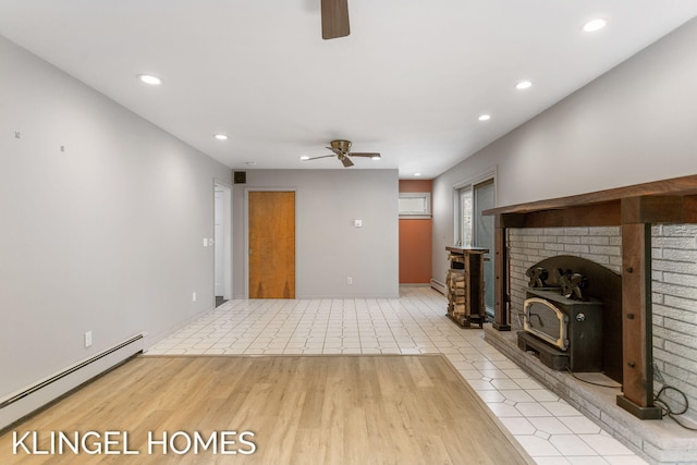 unfurnished living room featuring light hardwood / wood-style flooring, a wood stove, ceiling fan, and a baseboard radiator