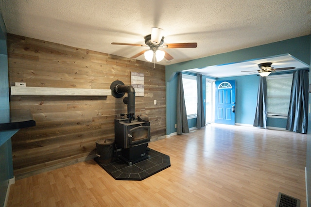 unfurnished living room with a wood stove, a textured ceiling, ceiling fan, wooden walls, and hardwood / wood-style floors