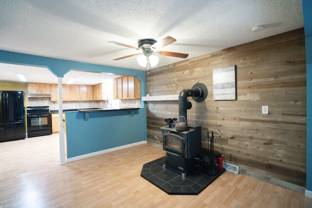 kitchen featuring light wood-type flooring, black appliances, kitchen peninsula, and wooden walls