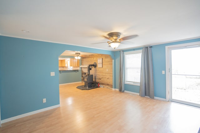 unfurnished living room with a wood stove, wood walls, ceiling fan, and light wood-type flooring