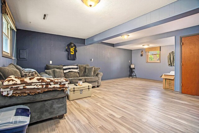 living room featuring light wood-type flooring, beam ceiling, a textured ceiling, and wood walls