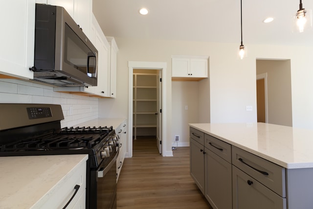 kitchen with light stone counters, stainless steel appliances, light hardwood / wood-style floors, white cabinetry, and decorative light fixtures