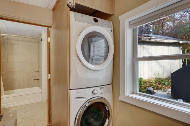 clothes washing area with light tile patterned floors, stacked washer / dryer, and a healthy amount of sunlight