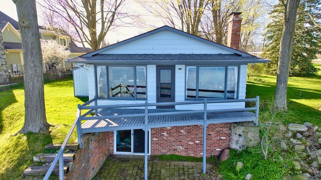 rear view of property featuring roof with shingles, a lawn, and a chimney