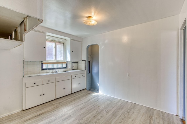 kitchen featuring decorative backsplash, light hardwood / wood-style floors, sink, and white cabinets