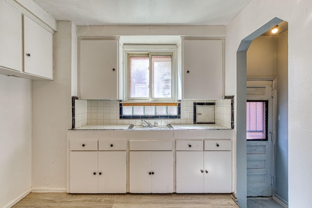 kitchen featuring light wood-type flooring, tile counters, sink, white cabinetry, and backsplash