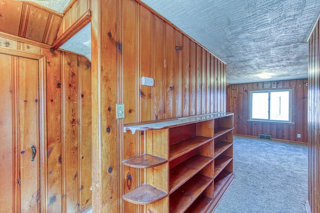 corridor featuring wooden walls, a textured ceiling, and carpet floors