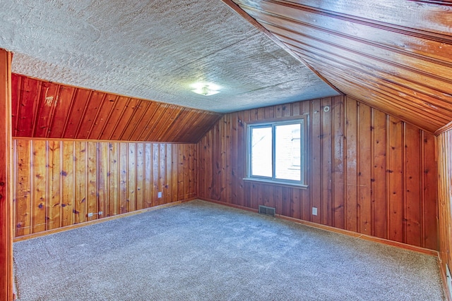 additional living space with carpet floors, lofted ceiling, and wood walls