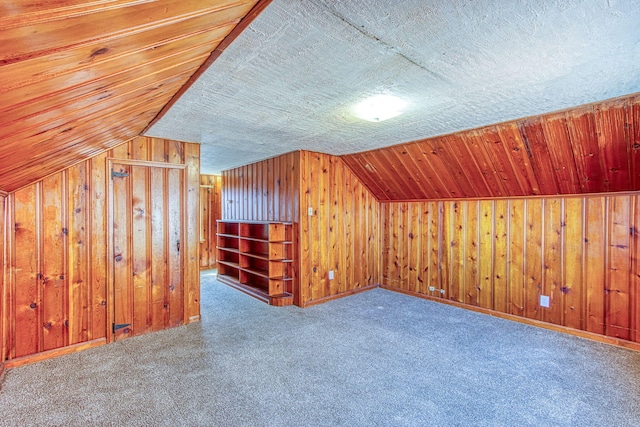 additional living space with wooden walls, vaulted ceiling, and carpet