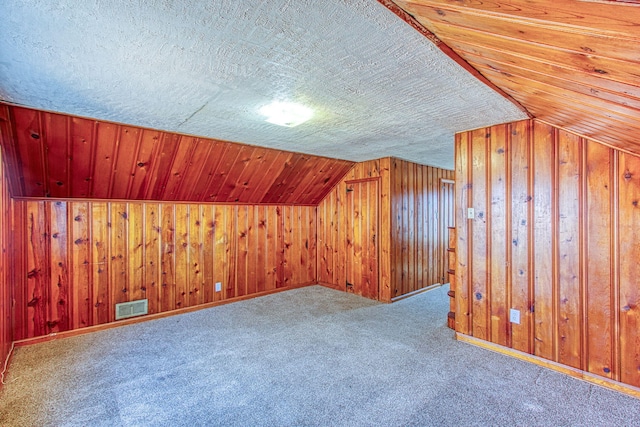 bonus room with wooden walls, lofted ceiling, a textured ceiling, and carpet