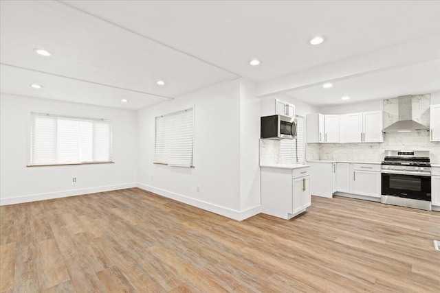 kitchen featuring white cabinets, wall chimney exhaust hood, stainless steel appliances, light hardwood / wood-style floors, and decorative backsplash