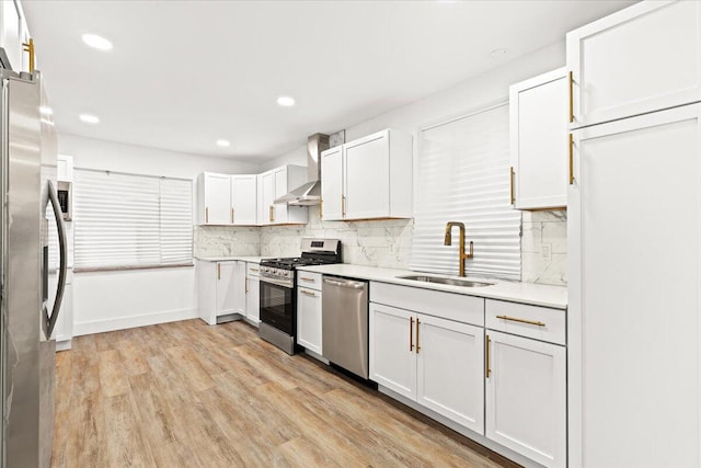 kitchen with sink, white cabinets, wall chimney range hood, light hardwood / wood-style flooring, and stainless steel appliances