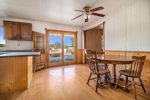 dining area featuring ceiling fan, light hardwood / wood-style flooring, wood walls, and a paneled ceiling