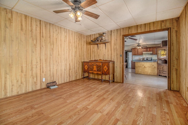 empty room featuring light hardwood / wood-style floors, wood walls, ceiling fan, and a drop ceiling