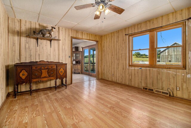 unfurnished room with ceiling fan, wooden walls, light wood-type flooring, and a healthy amount of sunlight