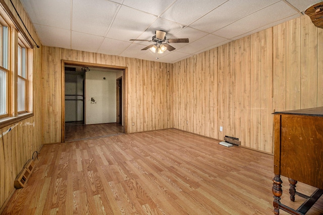 empty room with light hardwood / wood-style flooring, wood walls, and ceiling fan