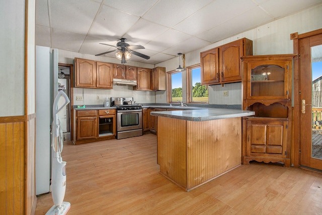 kitchen with kitchen peninsula, stainless steel stove, light wood-type flooring, ceiling fan, and sink