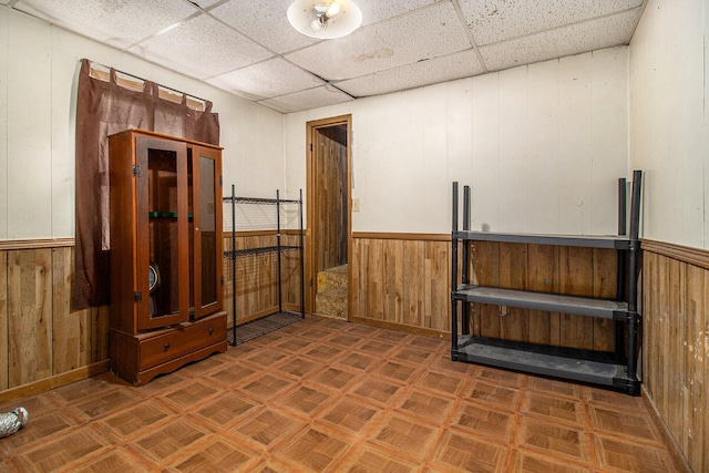 spare room featuring a drop ceiling, wooden walls, and dark parquet floors