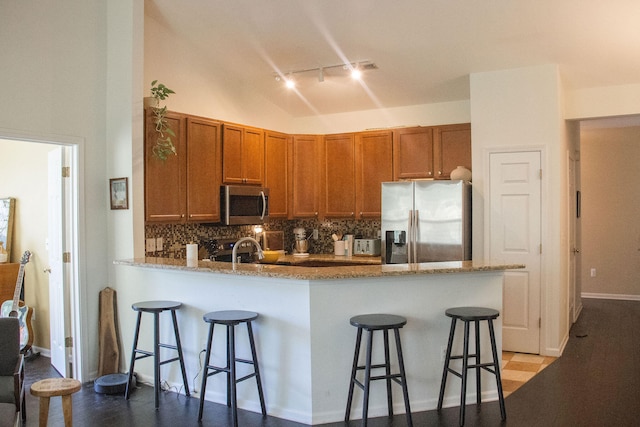 kitchen with wood-type flooring, a breakfast bar area, kitchen peninsula, backsplash, and appliances with stainless steel finishes